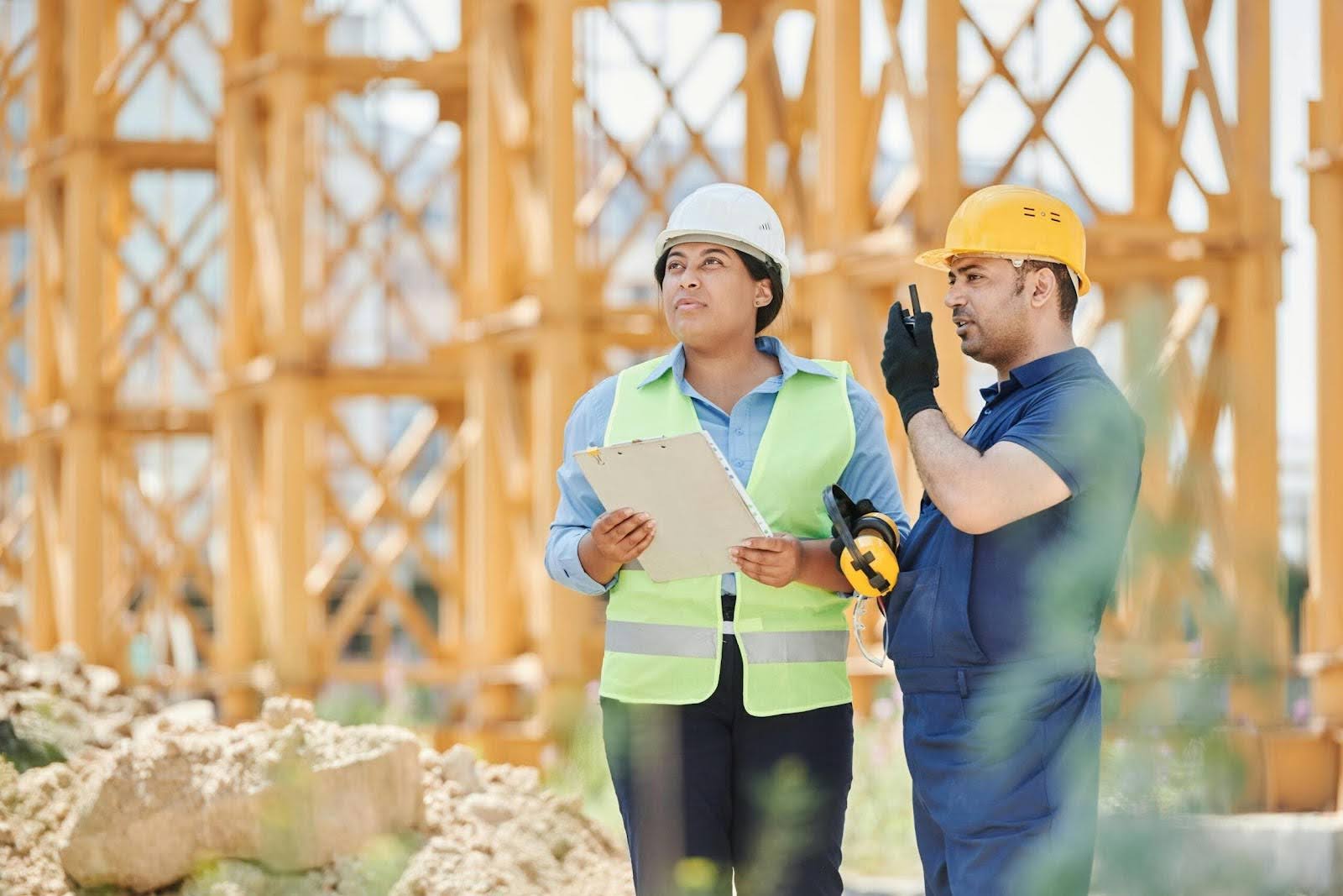 How Comprehensive Asbestos Surveys Can Save You from Legal Trouble, two people stanidng outside in hi vis vests and hart hats with a walkie talkie and clipboard